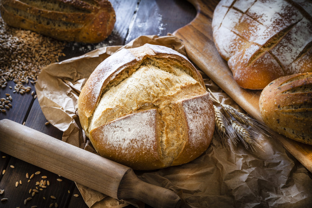Different types of bread shot on rustic wooden table. A fresh baked loaf of bread is on foreground on a brown craft paper. Predominant color is brown. Low key DSRL studio photo taken with Canon EOS 5D Mk II and Canon EF 100mm f/2.8L Macro IS USM